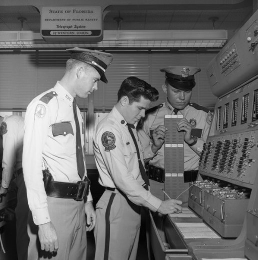 FHP Teletype Operator James Tubbs (center) shows Tallahassee City Police Wilton Dozier (left) and Billy Hudson (right) how to use the Teletype switching system for broadcasting messages to key Florida cities and relay through the nation.